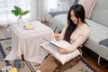 A beautiful young Asian woman using her digital tablet while relaxing in her living room Royalty Free Stock Photo