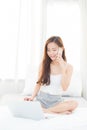 Beautiful young asian woman using laptop and talking smart mobile phone for leisure on bedroom Royalty Free Stock Photo