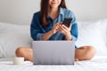 A beautiful young asian woman using mobile phone and laptop while sitting on a white bed Royalty Free Stock Photo