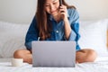 A beautiful young asian woman using and talking on mobile phone and laptop while sitting on a white bed Royalty Free Stock Photo