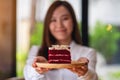 Blurred image of a young asian woman, waitress or a chef holding and serving a piece of red velvet cake in wooden tray Royalty Free Stock Photo