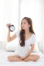 Beautiful young asian woman wake up in morning annoyed alarm clock holding hand Royalty Free Stock Photo
