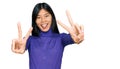 Beautiful young asian woman wearing casual clothes smiling with tongue out showing fingers of both hands doing victory sign Royalty Free Stock Photo