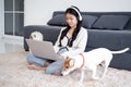 Beautiful young asian woman wearing headset sitting using laptop computer for music with companion dog. Royalty Free Stock Photo
