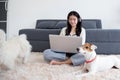 Beautiful young asian woman wearing headset sitting using laptop computer for music with companion dog. Royalty Free Stock Photo