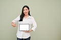 Beautiful Asian woman pointing finger at a tablet screen, standing against grey background Royalty Free Stock Photo