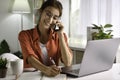 Beautiful young  Asian woman work at home with laptop and talking on smartphone and smiling. Female working on computer and using Royalty Free Stock Photo