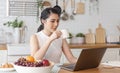 Beautiful young asian woman working on laptop computer while sitting at the kitchen room, drinking coffee Royalty Free Stock Photo