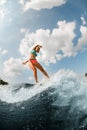 Young athletic woman in colorful swimsuit energetically balancing on wave on wakesurf board.
