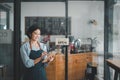 Beautiful young barista woman in apron holding order paper and standing in front of the door of cafe Royalty Free Stock Photo