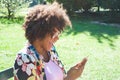Beautiful young black woman laughing and looking at the smartphone at the park