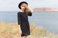 Beautiful young blond woman in a black dress and a light black hat in the desert and the wind blowing her hair in a hot summer day Royalty Free Stock Photo