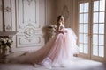 Beautiful young blond woman in luxurious long pink dress posing in vintage room interior