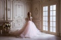 Beautiful young blond woman in luxurious long pink dress posing in vintage room interior Royalty Free Stock Photo