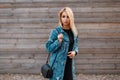 Beautiful young blond woman with a stylish leather handbag in a fashionable denim jacket in a black dress Royalty Free Stock Photo