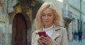 Beautiful young blond woman using phone in the old city center. Chatting with friends, girl using cellphone outdoors Royalty Free Stock Photo