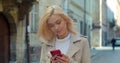 Beautiful young blond woman using phone in the old city center. Chatting with friends, girl using cellphone outdoors Royalty Free Stock Photo