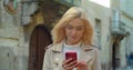 Beautiful young blond woman using phone in the old city center. Chatting with friends, girl using cellphone outdoors Royalty Free Stock Photo