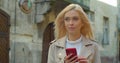 Beautiful young blond woman using phone in the old city center. Chatting with friends, girl using cellphone outdoors Royalty Free Stock Photo