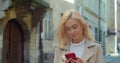 Beautiful young blond woman using phone in the old city center. Chatting with friends, girl using cellphone outdoors Royalty Free Stock Photo