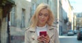 Beautiful young blond woman using phone in the old city center. Chatting with friends, girl using cellphone outdoors Royalty Free Stock Photo