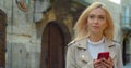 Beautiful young blond woman using phone in the old city center. Chatting with friends, girl using cellphone outdoors Royalty Free Stock Photo