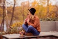 Beautiful young blonde in a brown warm sweater, black felt hat, blue jeans and boots sits on a bench in the autumn in the park, Royalty Free Stock Photo