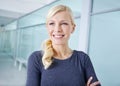 Beautiful young blonde businesswoman standing with her arms crossed in an office. One cheerful female businessperson at Royalty Free Stock Photo