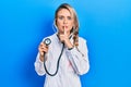 Beautiful young blonde doctor woman holding stethoscope asking to be quiet with finger on lips Royalty Free Stock Photo