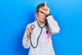 Beautiful young blonde doctor woman holding stethoscope making fun of people with fingers on forehead doing loser gesture mocking Royalty Free Stock Photo