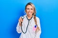 Beautiful young blonde doctor woman holding stethoscope sticking tongue out happy with funny expression Royalty Free Stock Photo