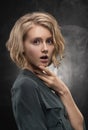 Beautiful young blonde girl with disheveled hairstyle and nude makeup, wearing a shirt and jeans emotionally posing on a gray Royalty Free Stock Photo