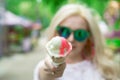 Beautiful, young blonde girl with ice cream in her hands, licks the ice cream on the background of a green park. Italian ice cream Royalty Free Stock Photo