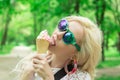 Beautiful, young blonde girl with ice cream in her hands, licks the ice cream on the background of a green park. Italian ice cream Royalty Free Stock Photo