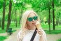 Beautiful, young blonde girl with ice cream in her hands, licks the ice cream on the background of a green park. Italian ice cream Royalty Free Stock Photo