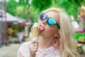 Beautiful, young blonde girl with ice cream in her hands, licks the ice cream on the background of a green park. Italian ice cream Royalty Free Stock Photo