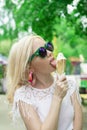 Beautiful, young blonde girl with ice cream in her hands, licks the ice cream on the background of a green park. Italian ice cream Royalty Free Stock Photo