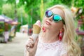 Beautiful, young blonde girl with ice cream in her hands, licks the ice cream on the background of a green park. Italian ice cream Royalty Free Stock Photo