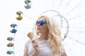 Beautiful, young blonde girl with ice cream in her hands, licks the ice cream on the background of a green park. Italian ice cream Royalty Free Stock Photo