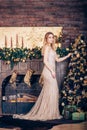 Beautiful young blonde girl in a long Golden dress smiling and decorating the Christmas tree near the fireplace Royalty Free Stock Photo