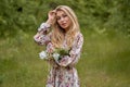 Beautiful young blonde girl with long hair in a long dress with a floral print posing with a flower in her hand Royalty Free Stock Photo