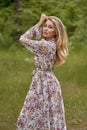 Beautiful young blonde girl with long hair in a long dress with a floral print posing with a flower in her hand Royalty Free Stock Photo