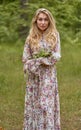 Beautiful young blonde girl with long hair in a long dress with a floral print posing with a flower in her hand Royalty Free Stock Photo