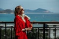 Beautiful young blonde girl in red dress and sunglasses drinking red cocktail from a glass on balcony. Against the Royalty Free Stock Photo
