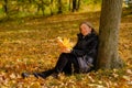 A beautiful young blonde girl sits on fallen autumn leaves in the park Royalty Free Stock Photo