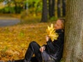 A beautiful young blonde girl sits on fallen autumn leaves in the park Royalty Free Stock Photo