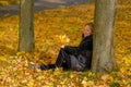 A beautiful young blonde girl sits on fallen autumn leaves in the park Royalty Free Stock Photo