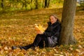 A beautiful young blonde girl sits on fallen autumn leaves in the park Royalty Free Stock Photo