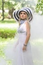 Beautiful young blonde girl with a striped hat and a white dress in the forest covered in smoke Royalty Free Stock Photo