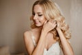 Beautiful and young blonde model woman, with wedding hairstyle and professional bright makeup, adjusting her earring at Royalty Free Stock Photo